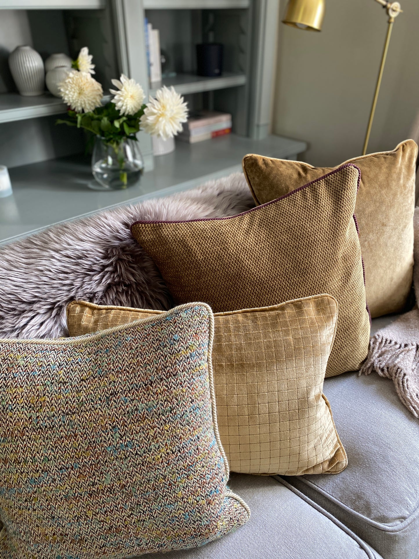 Woven cushion sitting along side 3 textured gold velvet cushions on a sofa