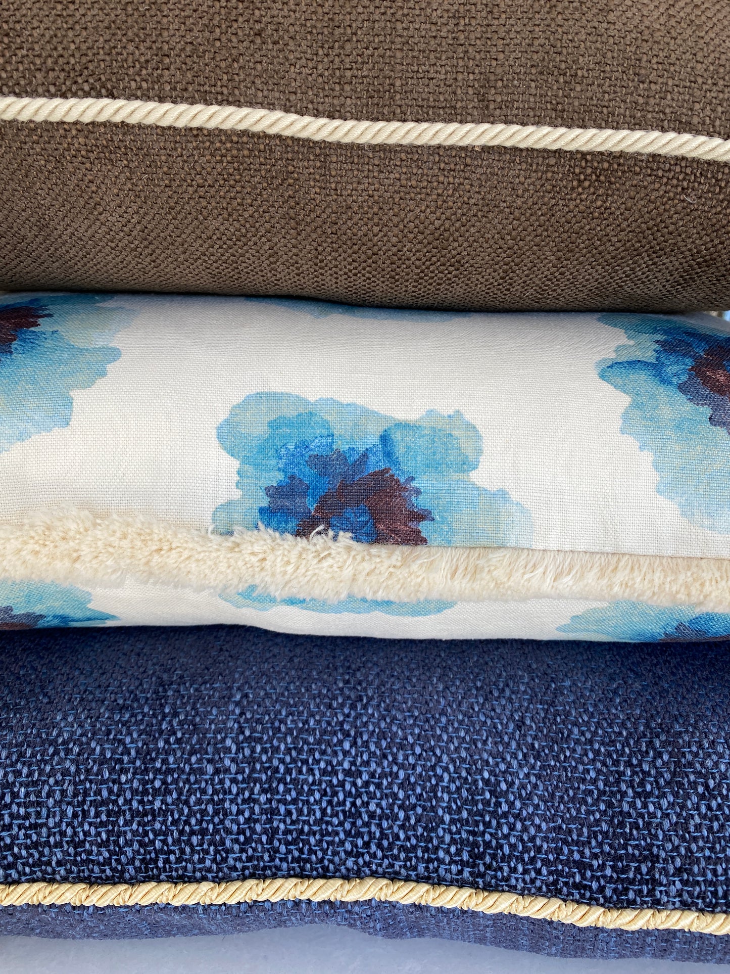 Close-up of three textured cushions - a brown a navy and a floral linen cushion all with decorative trims
