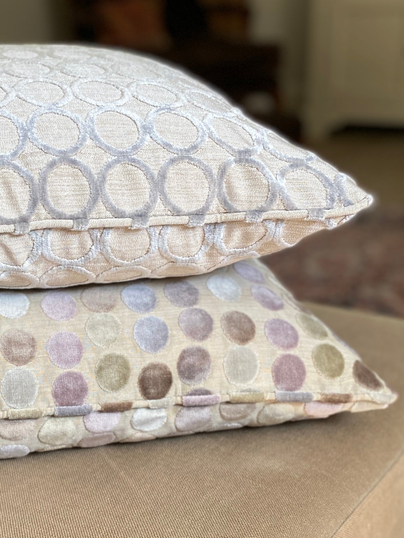 Two velvet cushions lying on top of each other, one with a hollowed out circle design and one with pastels coloured dots and both with self piping.