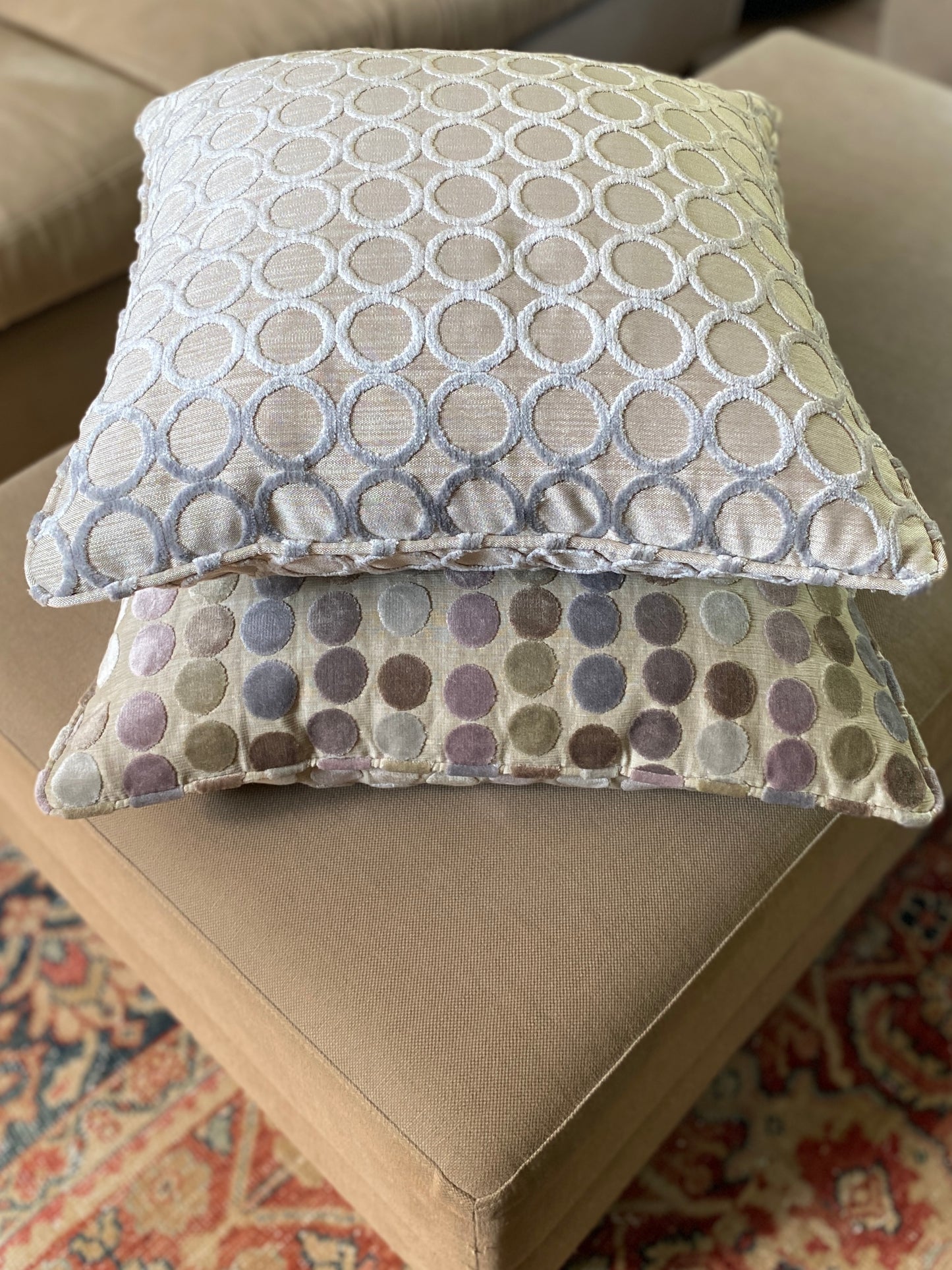 Two velvet cushions lying on top of each other, one with a hollowed out circle design and one with pastels coloured dots and both with self piping.