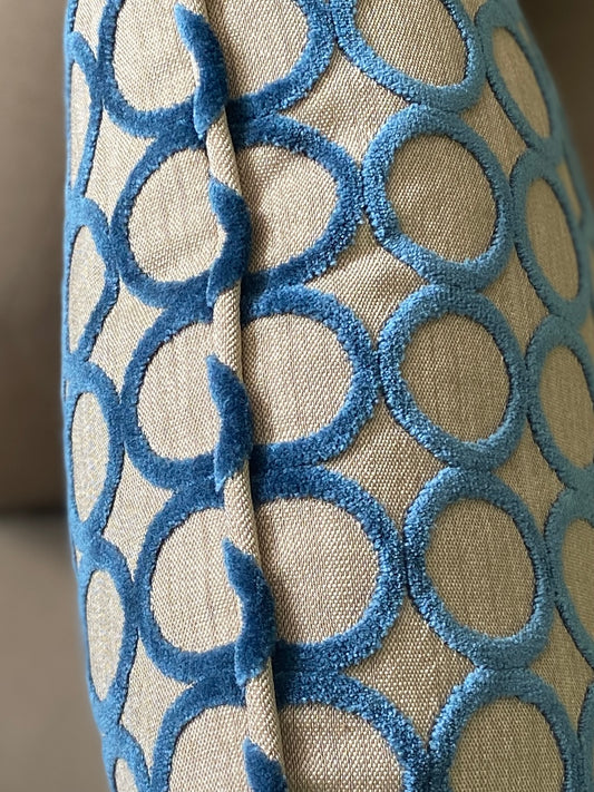 Close up of the piping on a cut pile velvet cushion showing circles in teal velvet and a beige background.
