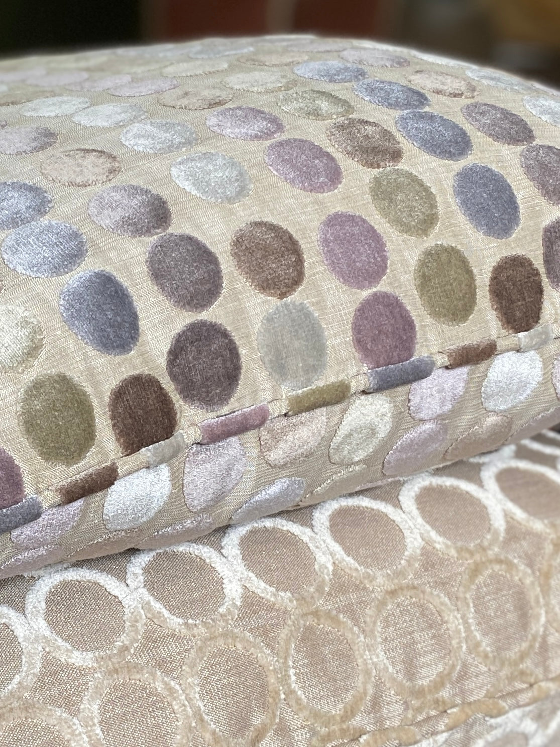 Close up of two circle design cut pile velvet cushions with piped edges in pastels and taupe with beige backgrounds