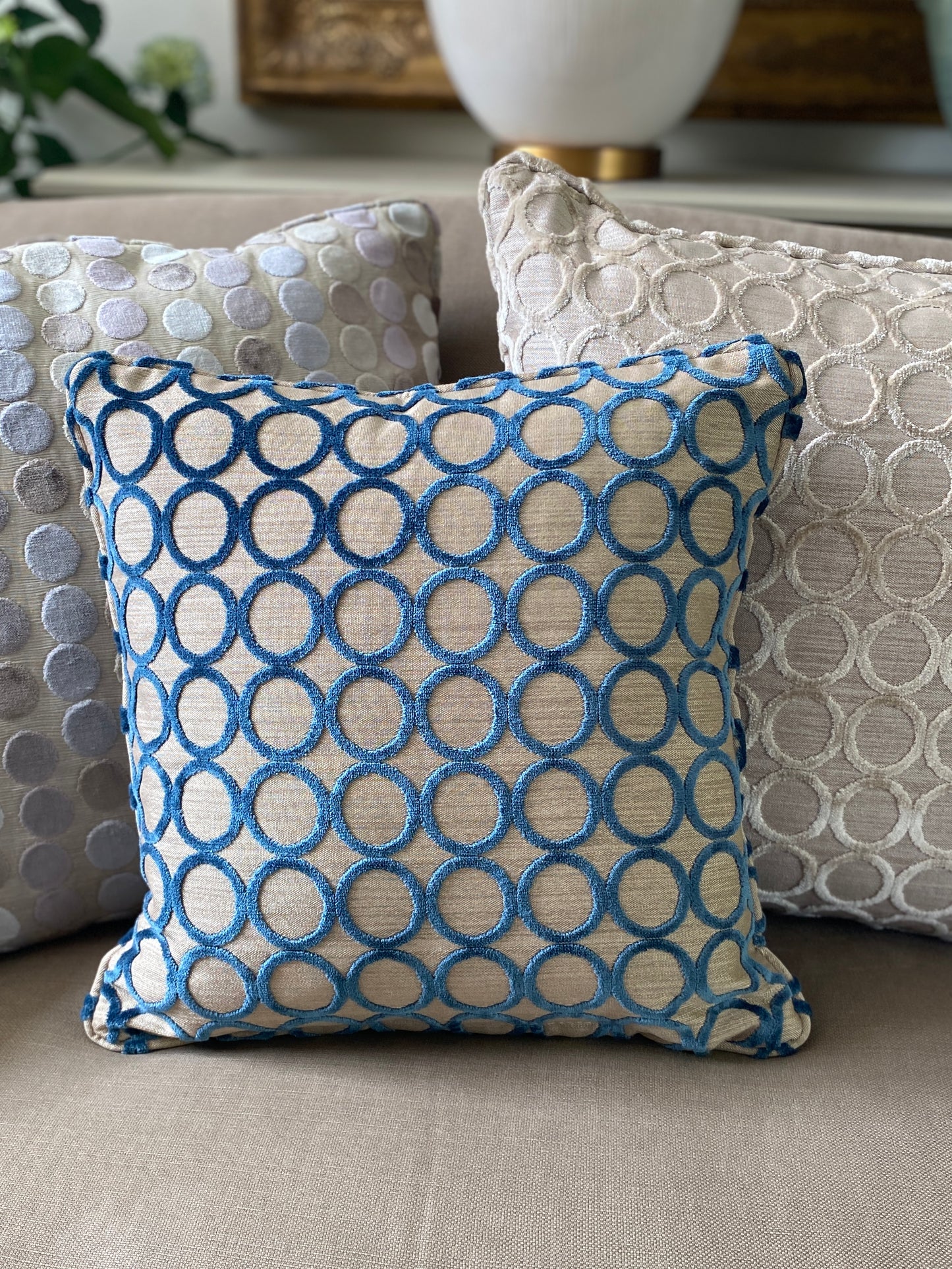 3 square cushions in cut pile velvets, 2 with circle designs in teal and taupe and one with pastel dots.