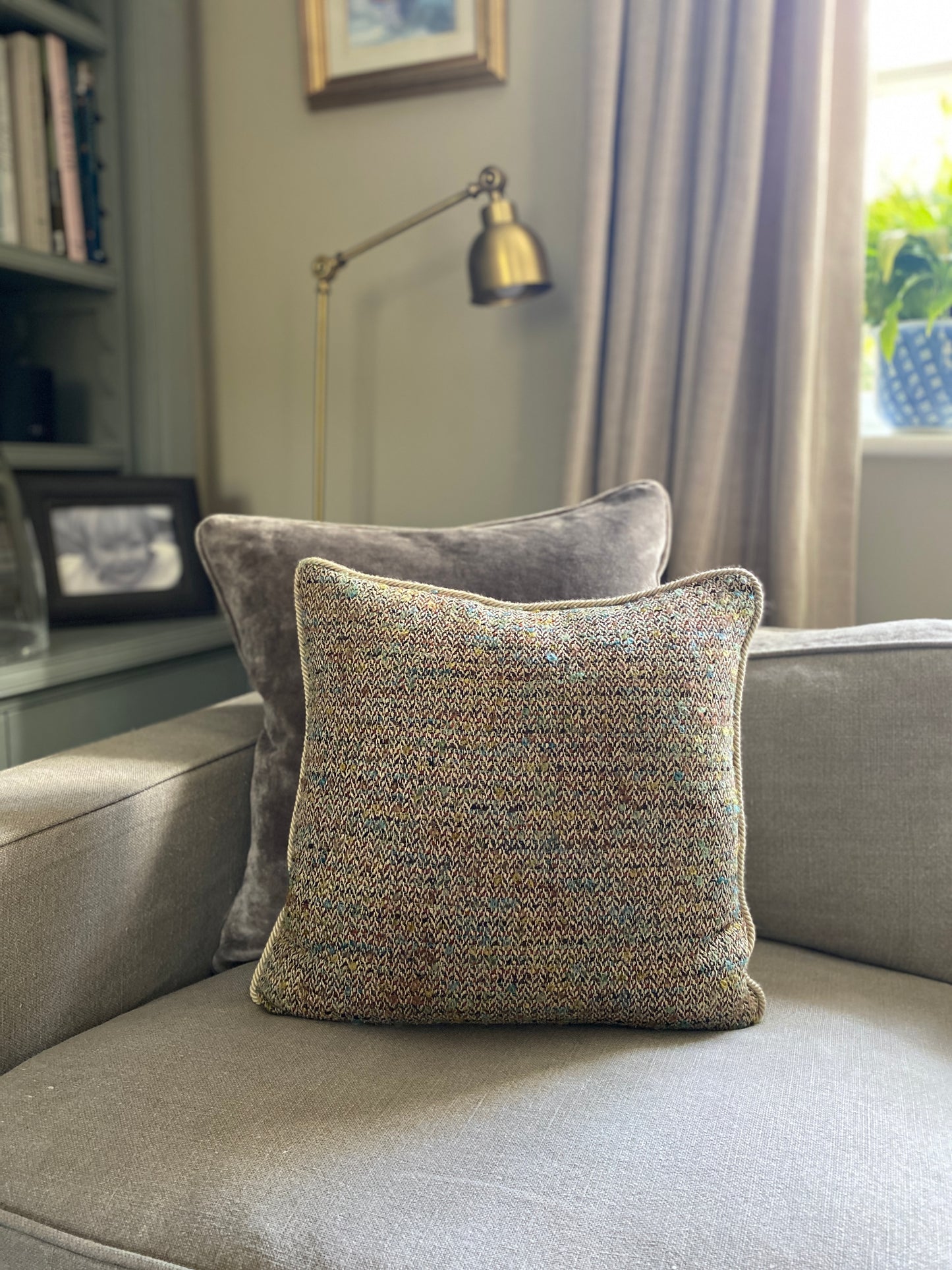 Woven cushion on a sofa in front of a grey velvet cushion.