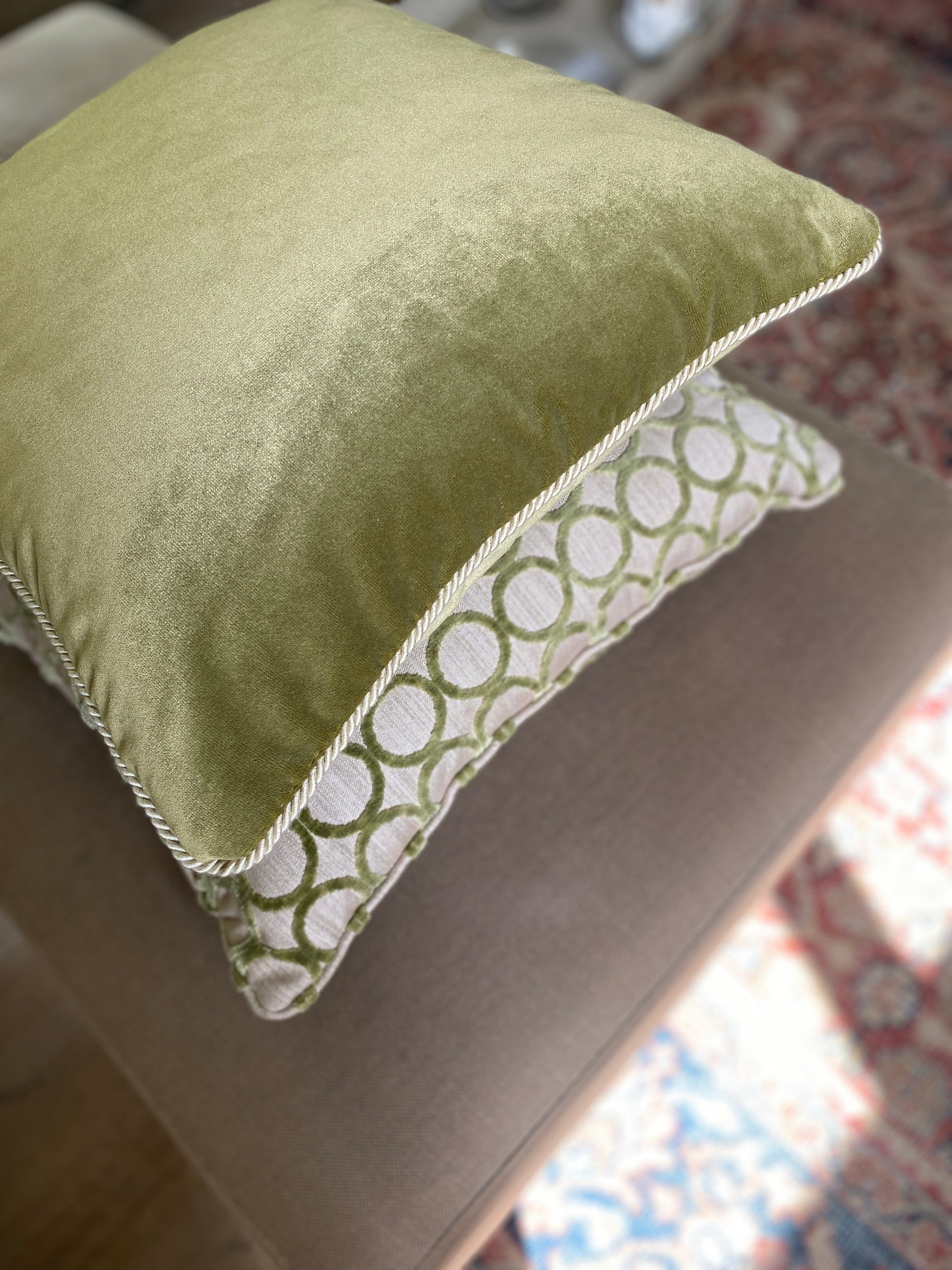 Overhead shot showing moss green velvet square cushion on top of a cut pile velvet square cushion in green with a circle design.