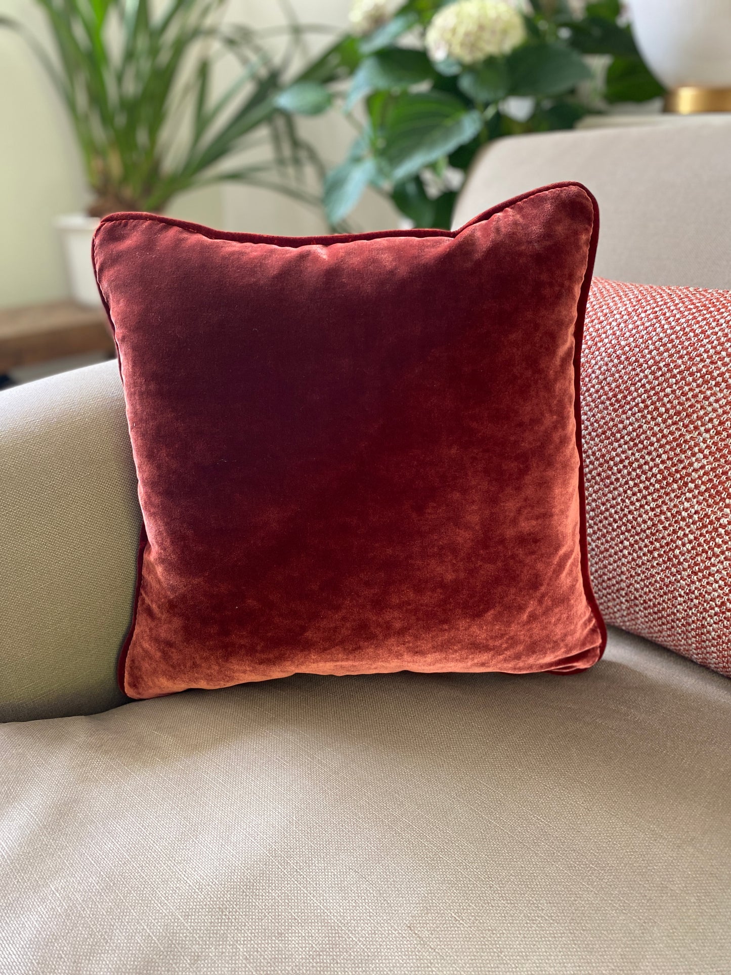 Chestnut velvet square cushion measures 38cm x 38cm and has self piping around the edges. Is shown partnering with a woven rectangular cushion