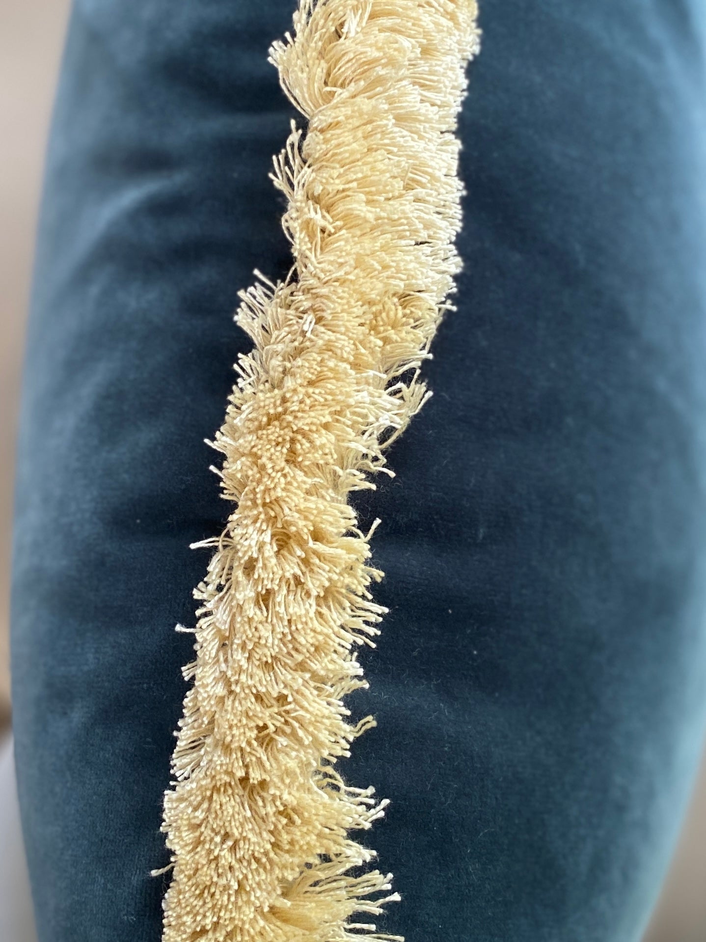 Close up of teal velvet cushion with complimentary natural fringing.