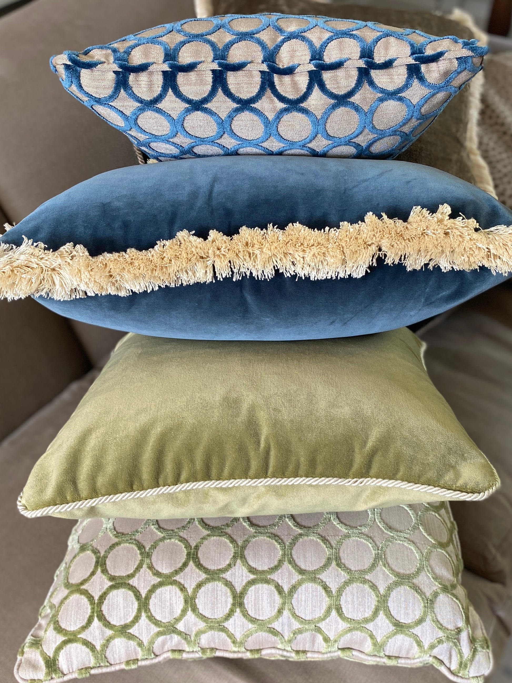 Pile of 4 cushions with a close up on the trim styles, showing natural cord, fringing, and self piping.