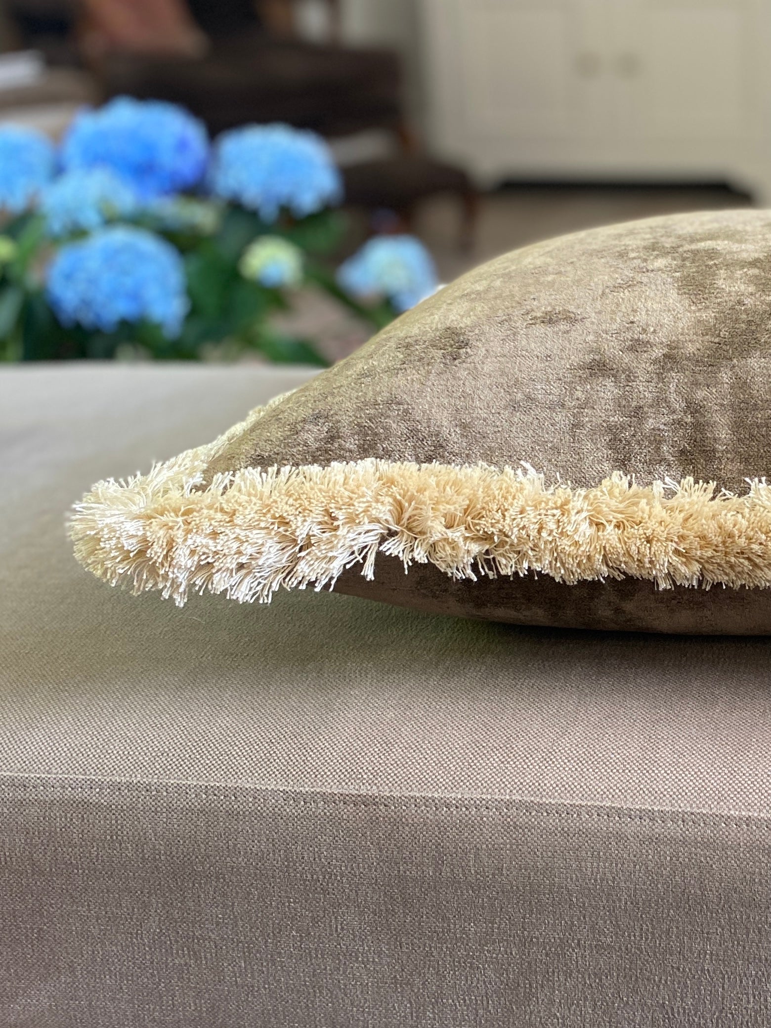 Close up of brown vintage feel velvet cushion with cream fringing lying down.