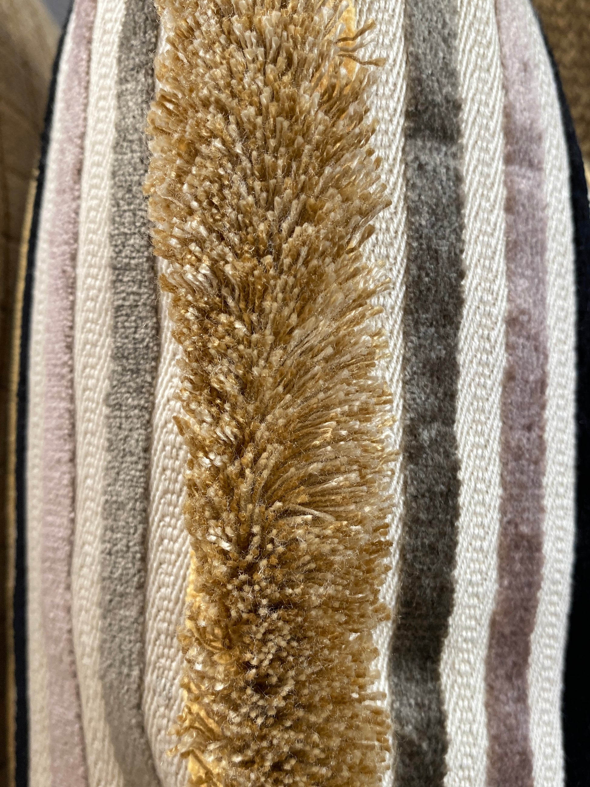 Close-up of a cushion with a gold fringe on a striped background