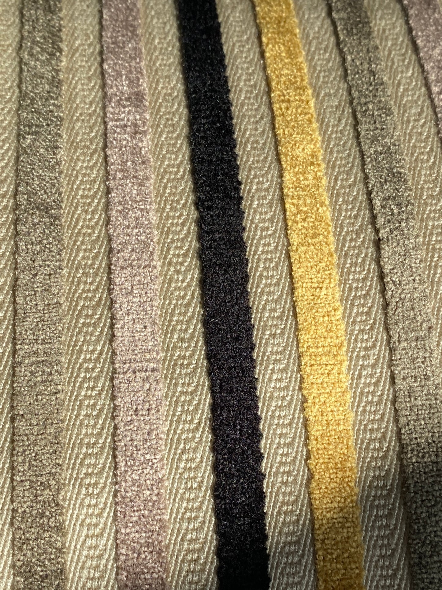 Close up of cushion fabric showing stripes in gold, black, and browns on a beige background