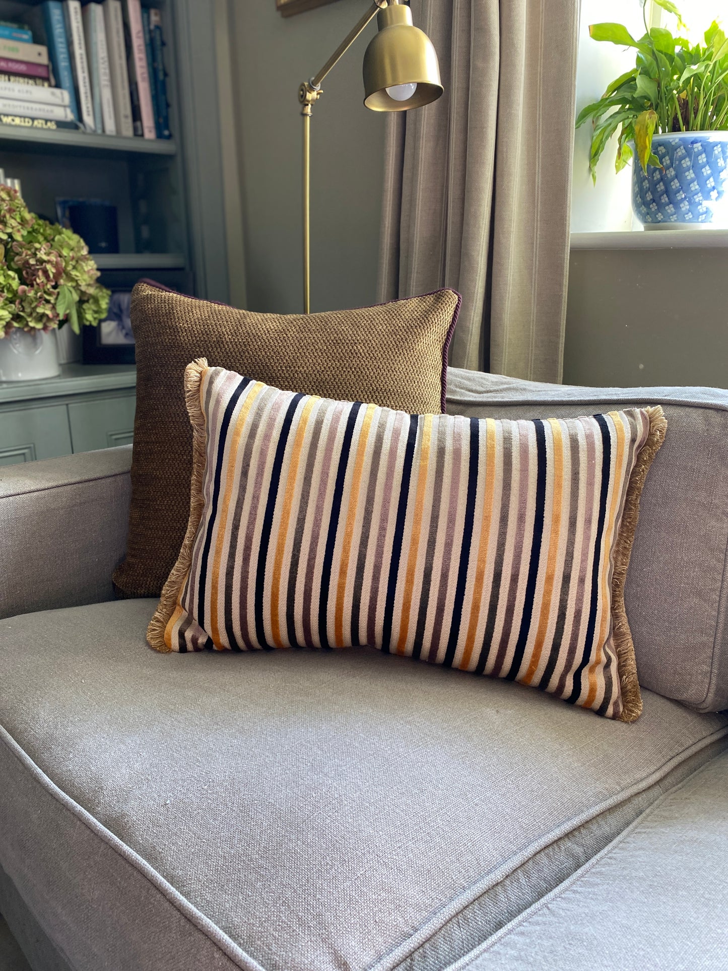 Striped cushion on a grey sofa with a lamp and books in the background