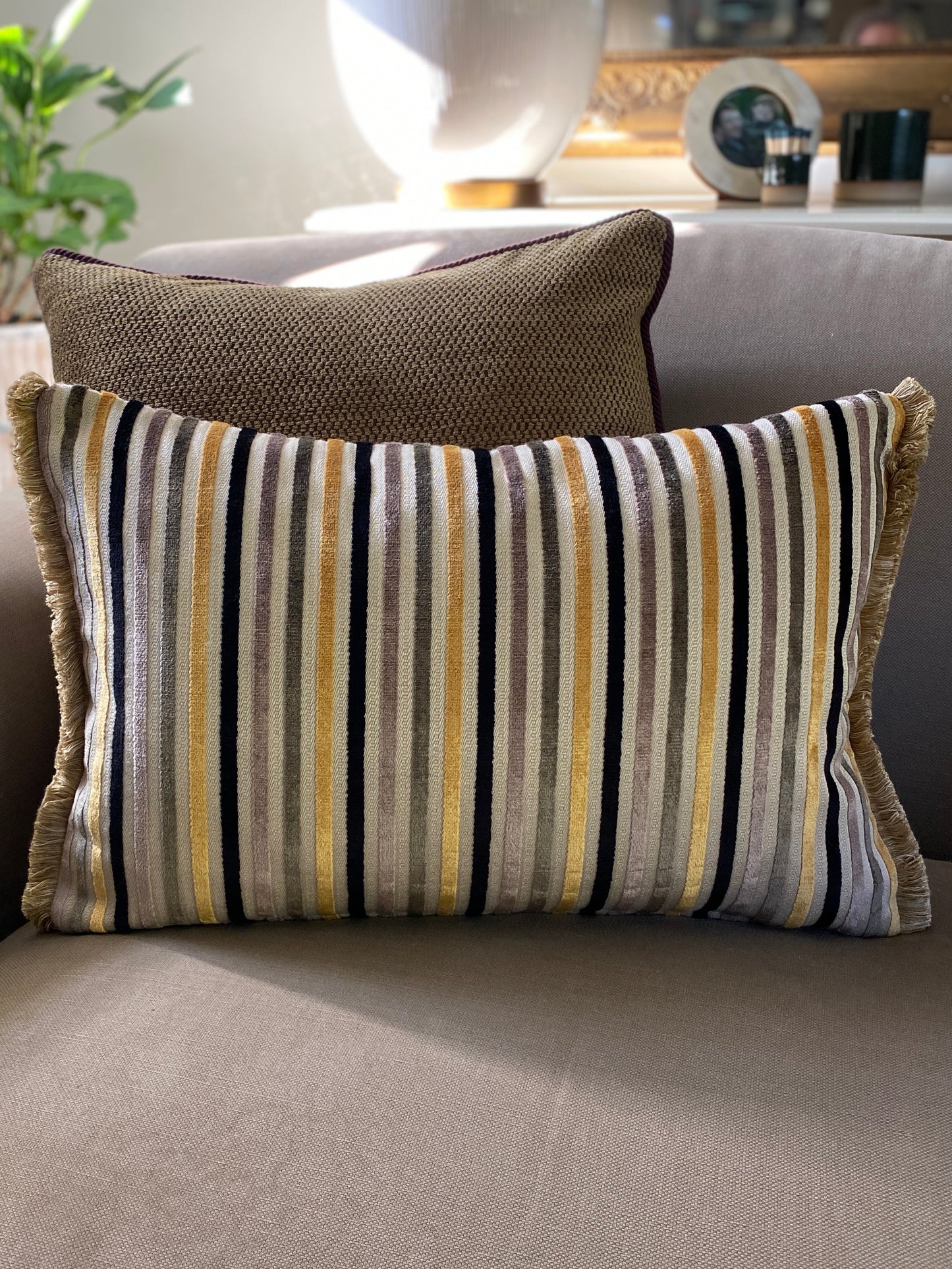 Striped cushion with fringing on the rectangle ends on a sofa with a neutral background
