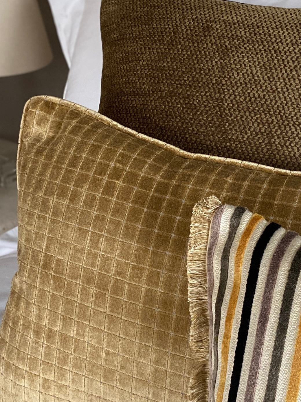 Cushions on a bed in textured golden velvets and a striped cushion