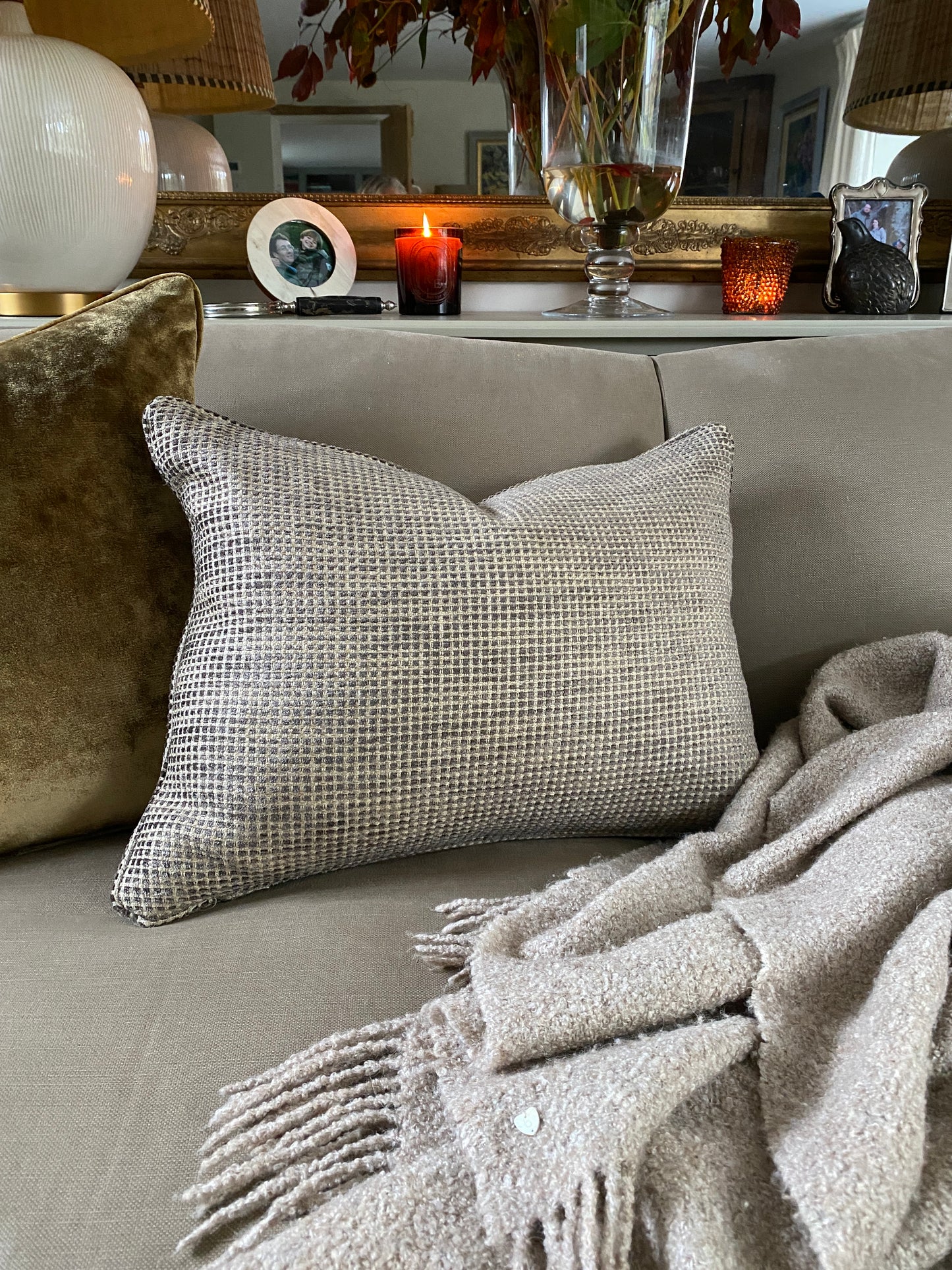 Rectangular chenille cushion in earthy browns with a sand coloured background sitting next to an antique gold velvet cushion on a sofa.