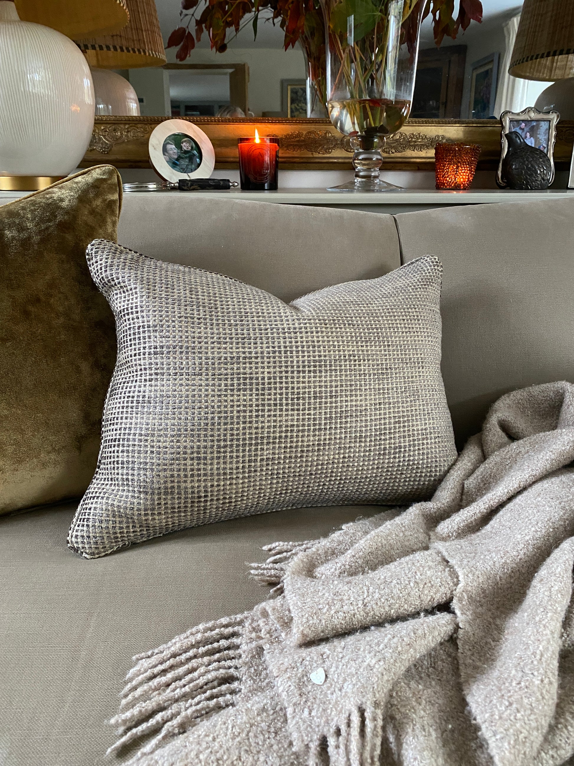 Rectangular chenille cushion in earthy browns with a sand coloured background sitting next to an antique gold velvet cushion on a sofa.