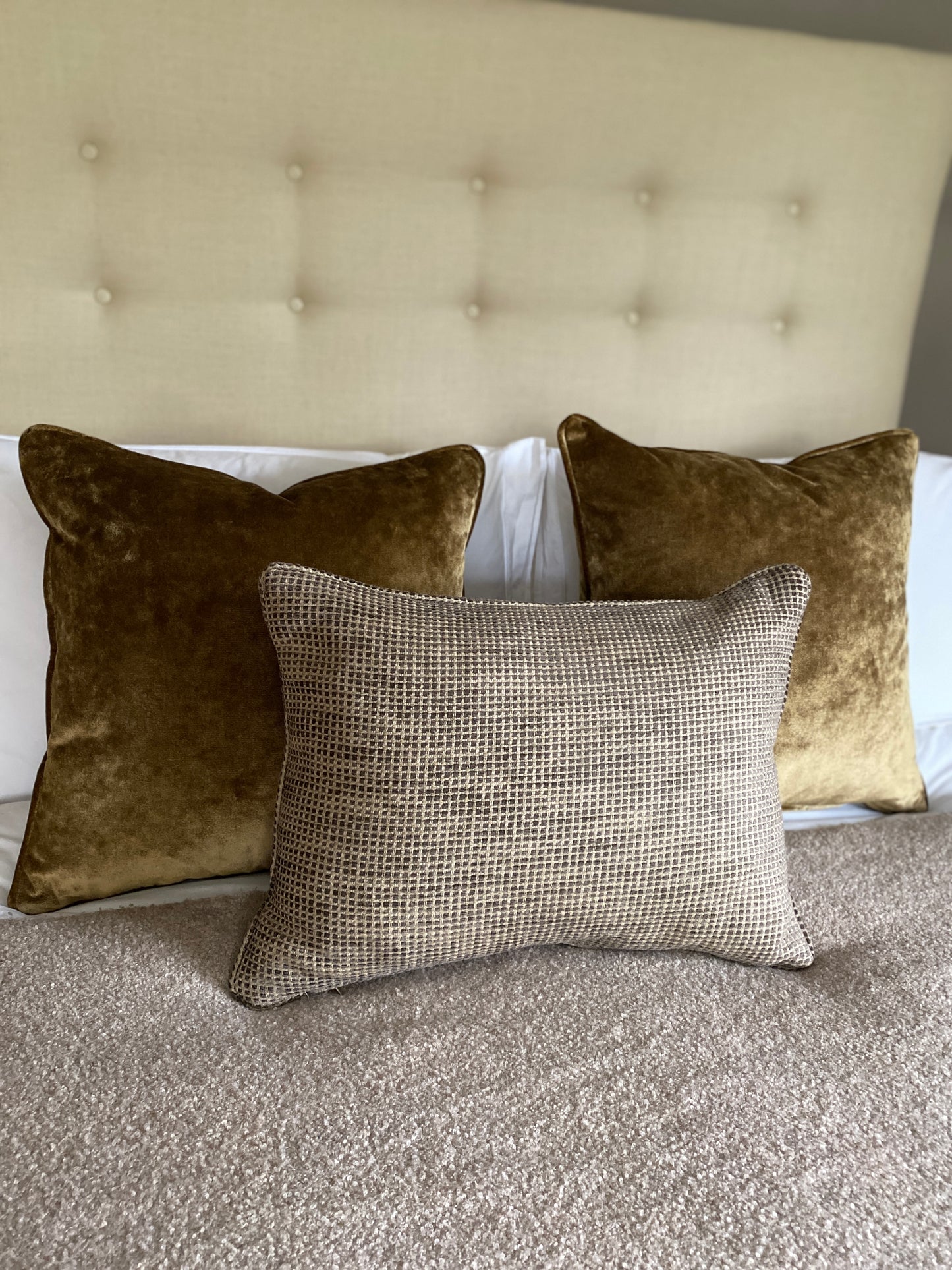 Earthy brown textured chenille cushion in front of two antique gold velvet cushions on a bed.