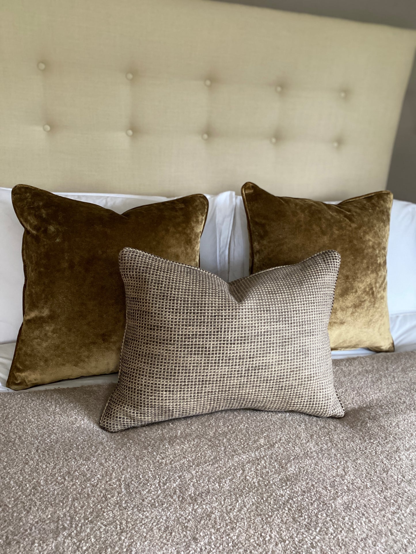 Two antique gold cushions on a bed paired with a rectangular chenille cushion in browns.