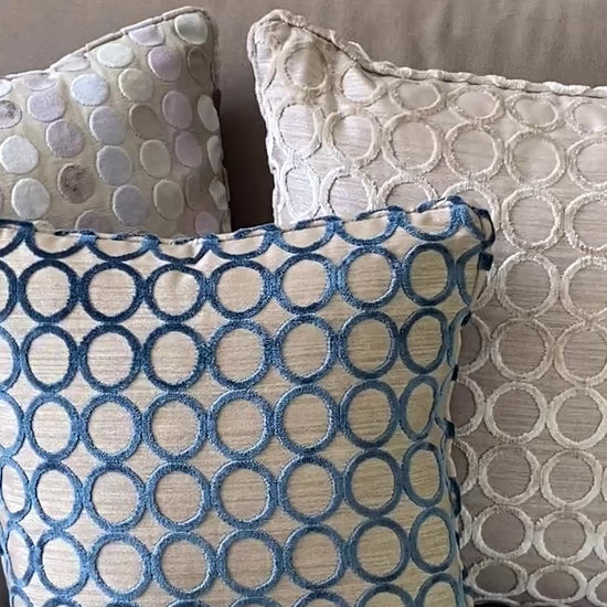 3 square cushions in cut pile velvets, 2 with circle designs in teal and taupe and one with pastel dots.
