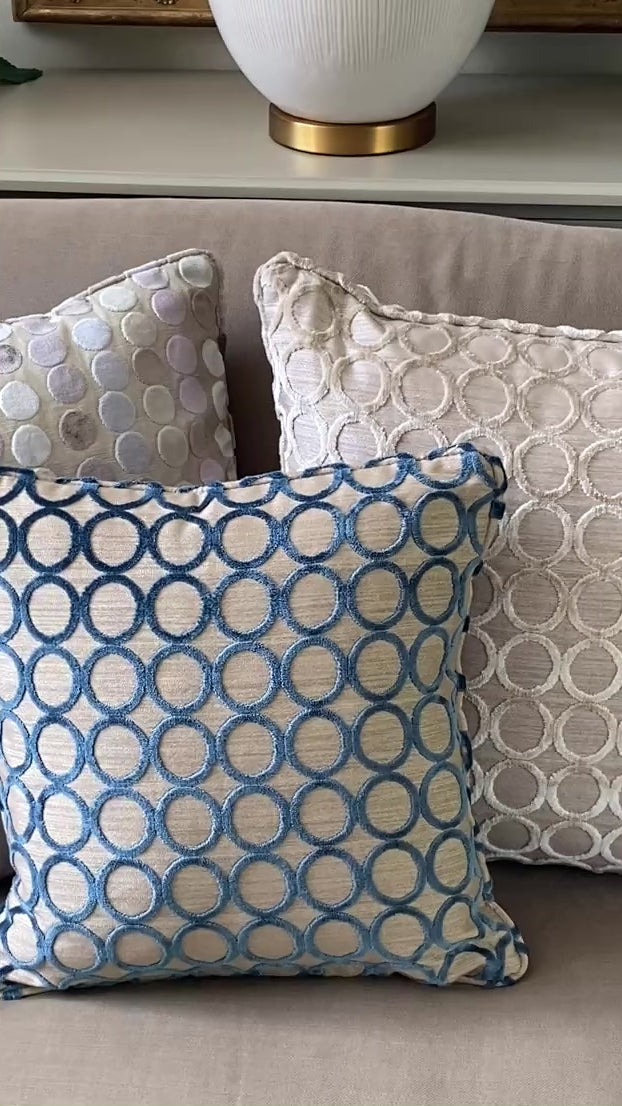 3 square cushions in cut pile velvets, 2 with circle designs in teal and taupe and one with pastel dots.